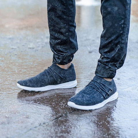A close-up image of a man’s legs standing in the rain, wearing Vessi eco-friendly shoes.